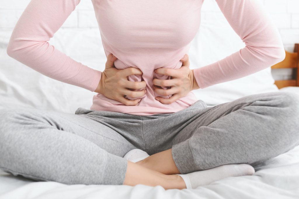 Woman suffering from abdominal pain, sitting in bed
